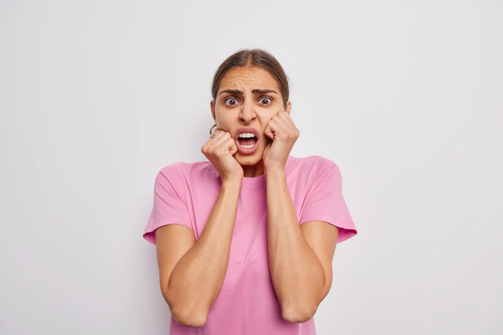 Indoor shot of scared irritated young woman looks with fearful horrified expression reacts on something unpleasant dressed in casual pink t shirt isolated over white background. Human reactions Fuga de talento